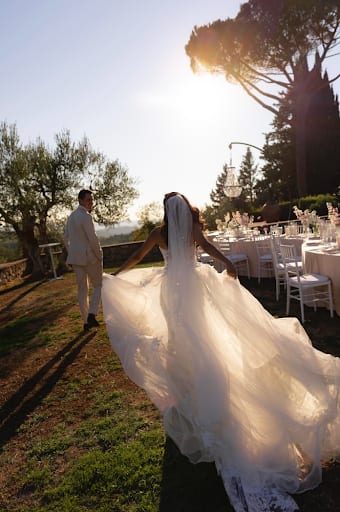 Sarah crossing the lawn at golden hour, veil catching the light, guests' tables set under the Tuscan pines behind her